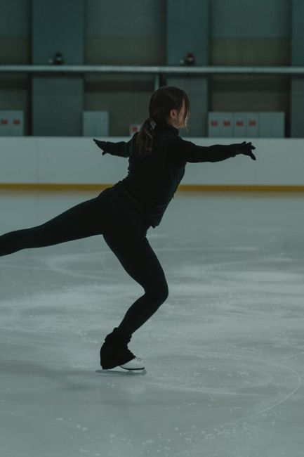 A woman in black performs a figure skating routine indoors, showcasing a beautiful spin.