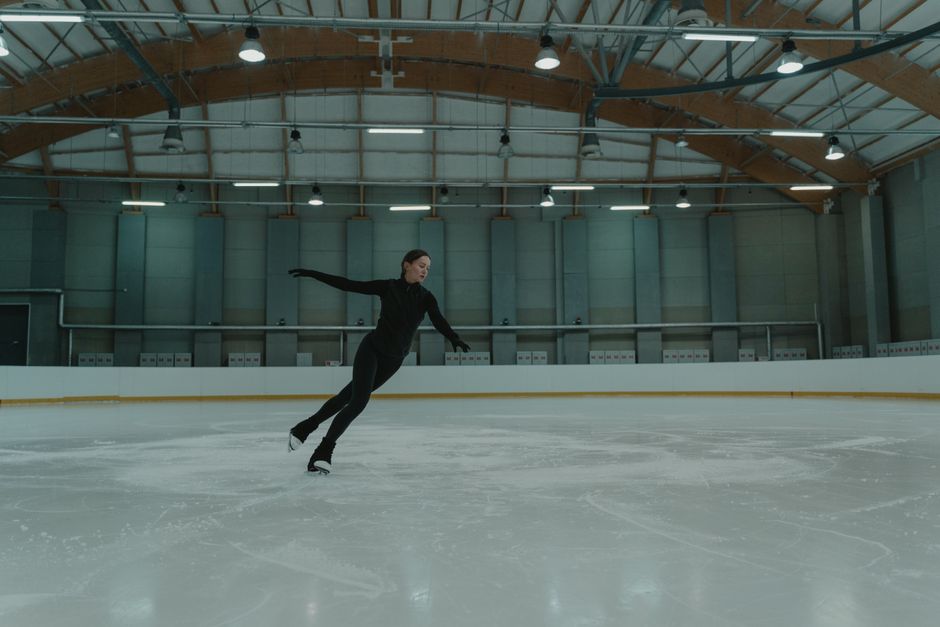 A female figure skater practices on an indoor ice rink, showcasing skill and balance.