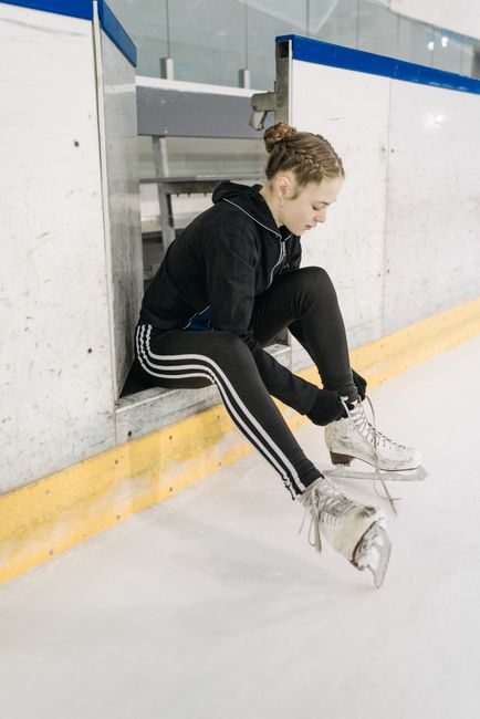 Young figure skater tying ice skates before training on an indoor ice rink.