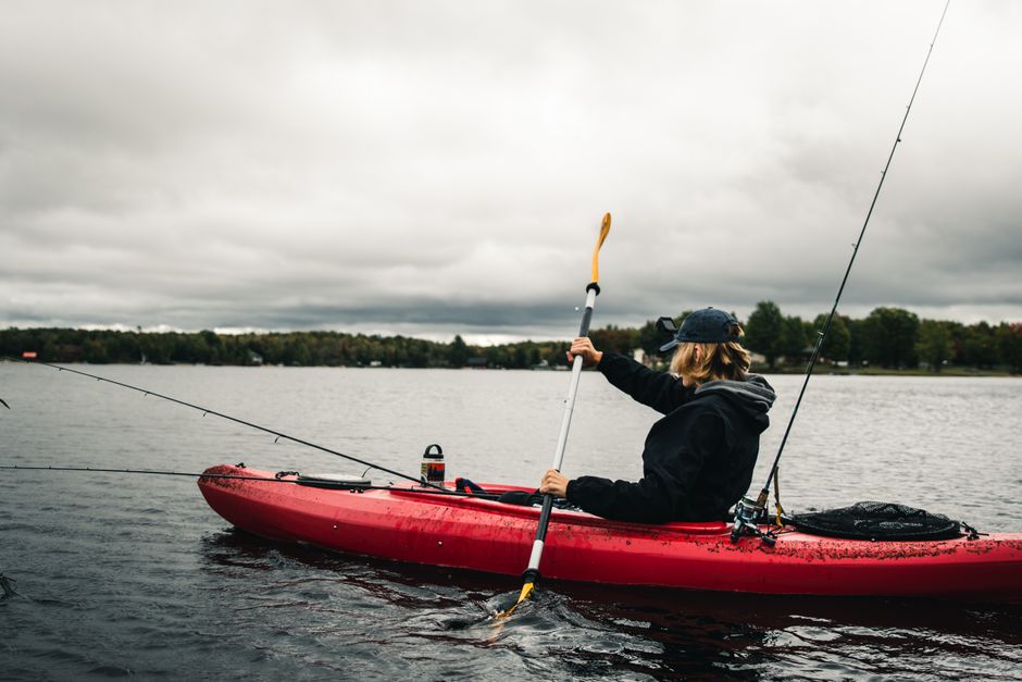 A person kayaking and fishing on a serene lake under overcast skies.