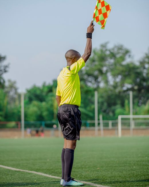 Soccer referee signaling offside with flag on a sunny day on the field.