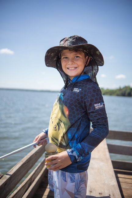 Smiling boy fishing with a rod on a sunny day at a lake in Brazil. Outdoor fun and adventure.