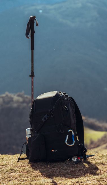 Black backpack and trekking pole on a grassy hill with mountain views, perfect for adventure.