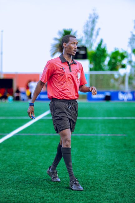 Soccer referee wearing red officiates a game on a vibrant green field.