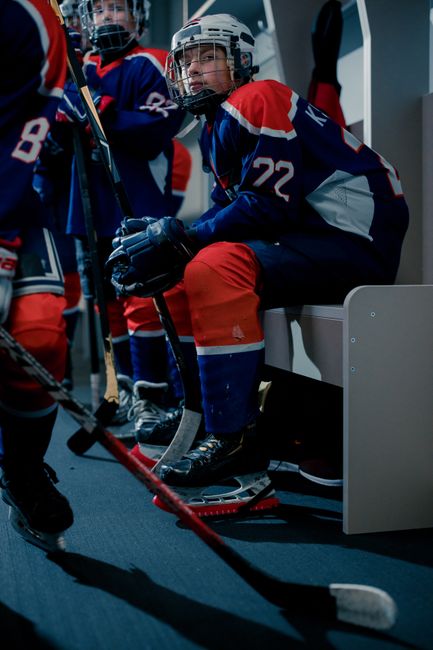 Teen hockey players in full gear prepare for a game in a locker room setting.