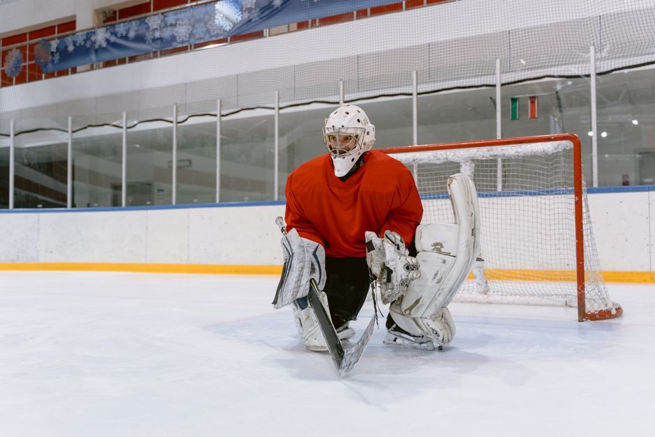 Ice hockey goaltender in red jersey at the rink, ready to defend the goal.