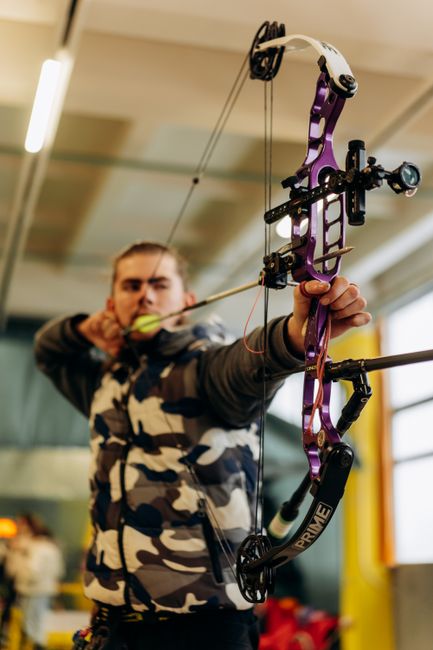 A man intensely focuses on aiming a purple compound bow at an indoor archery range.