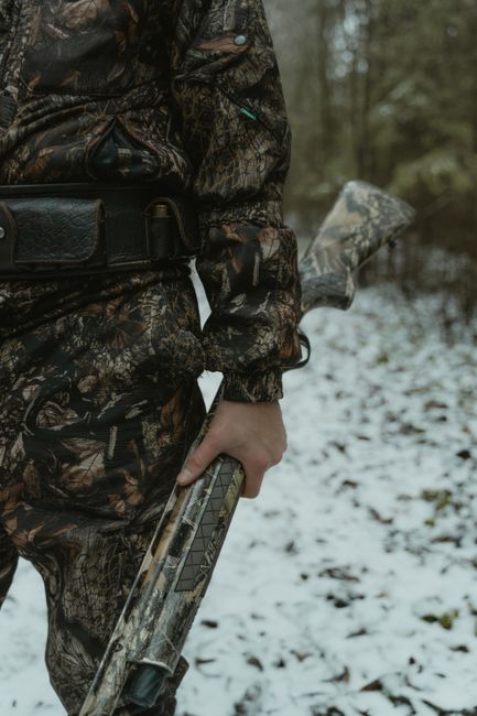 A person in camouflage holding a shotgun in a snowy forest setting.