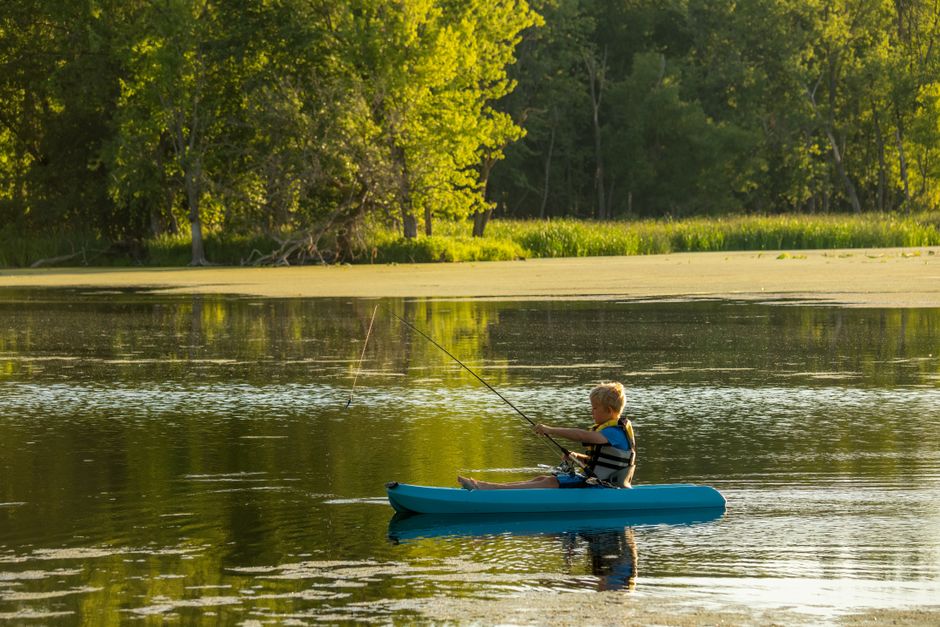 A young boy paddles a kayak while fishing on a serene Minnesota lake, enjoying nature.