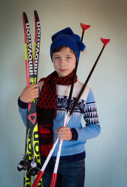 A young boy in winter attire holding skis and poles, ready for skiing adventure.