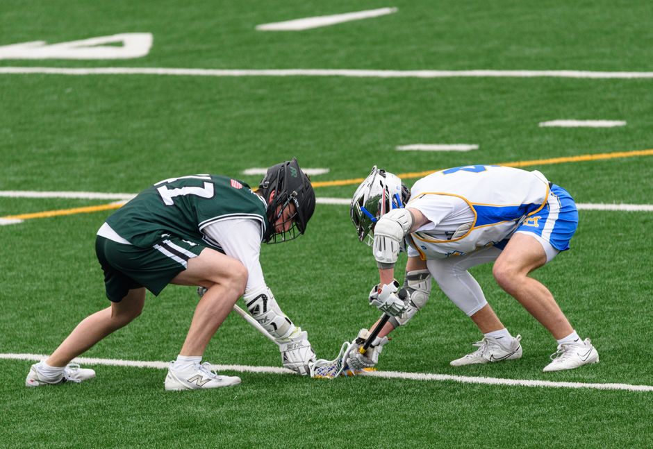 Two lacrosse players face-off on a vibrant green field, showcasing the sport's intensity and skill.