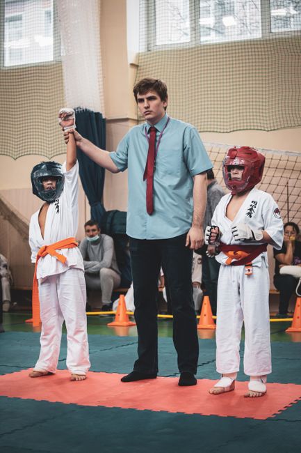 A referee declares the winner among two young karate participants in a sports event.