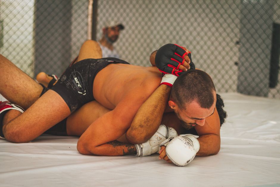 Intense moment of MMA fighters grappling inside an indoor cage.