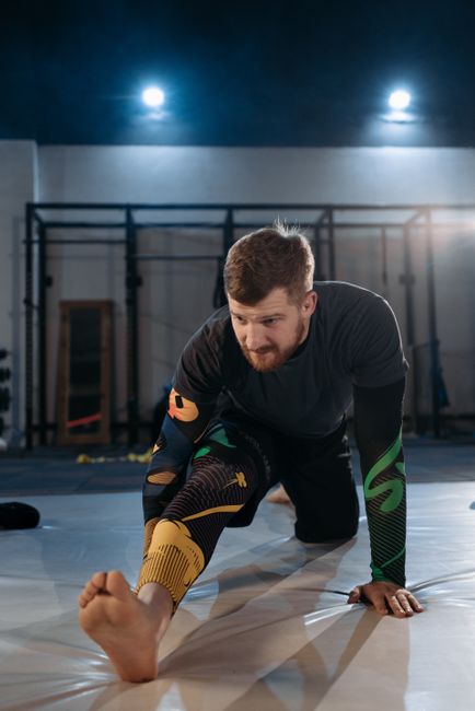 Focused MMA fighter stretches on the gym mat during training session.