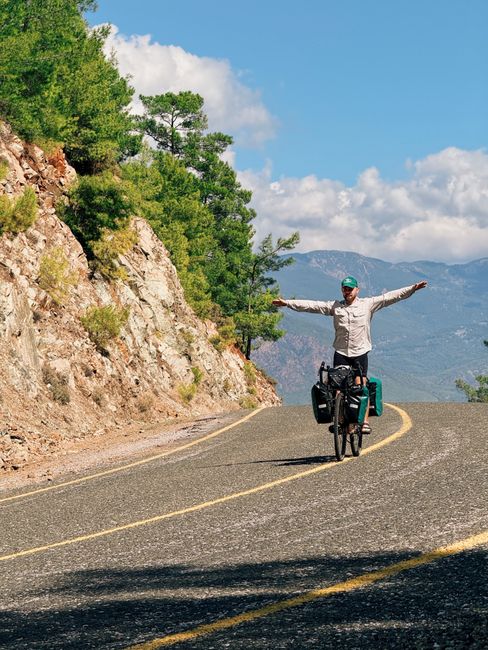 A cyclist balances on a mountain road amidst scenic nature vistas.