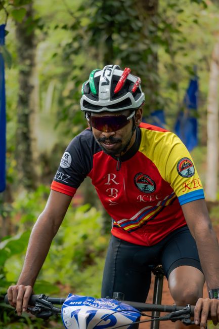 Mountain biker wearing racing gear competes in a lush green forest trail.