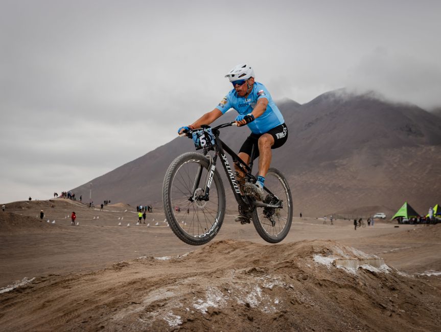 A cyclist in action jumping on a mountain bike in a desert setting during daytime.