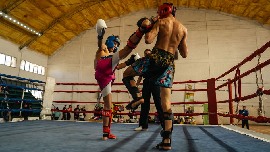 Two fighters engaged in a dynamic Muay Thai match inside a sports arena.