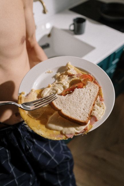Person holding a plate with a croque madame sandwich featuring cheese, ham, and tomatoes.