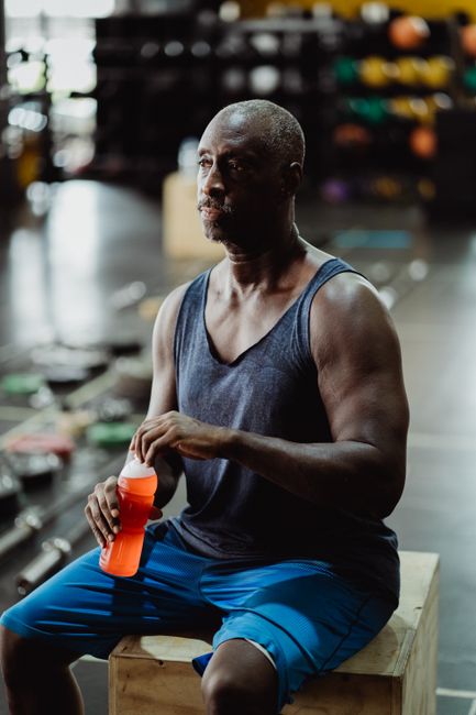 Fit African American man taking a break, holding a protein shake in a modern gym setting.