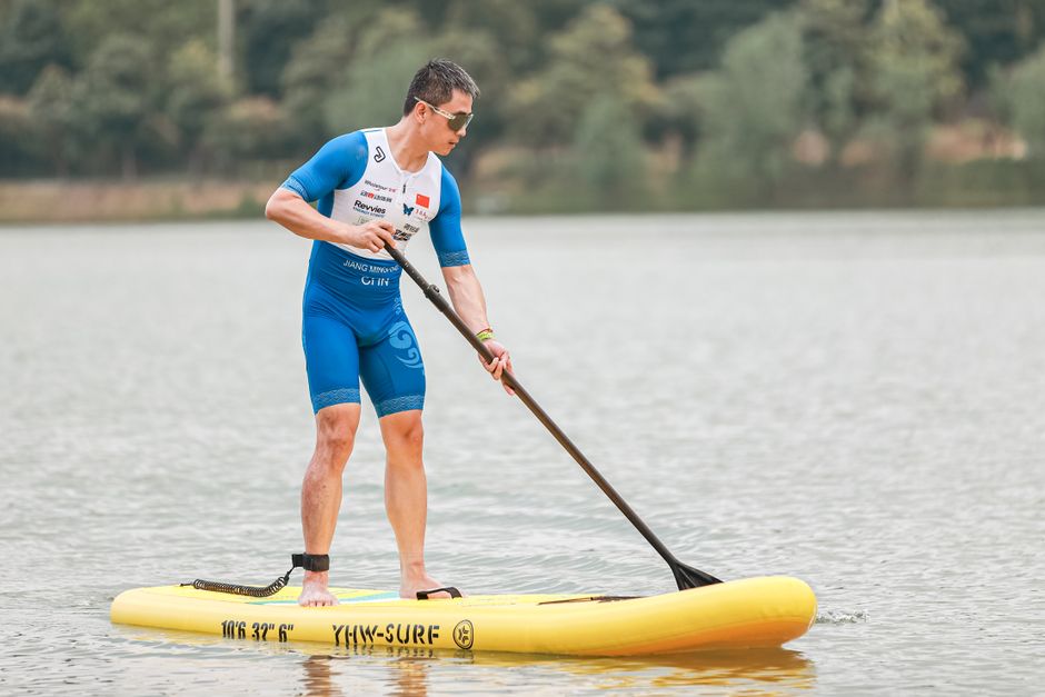 A man in sportswear paddleboarding on a tranquil lake, embodying outdoor fitness.