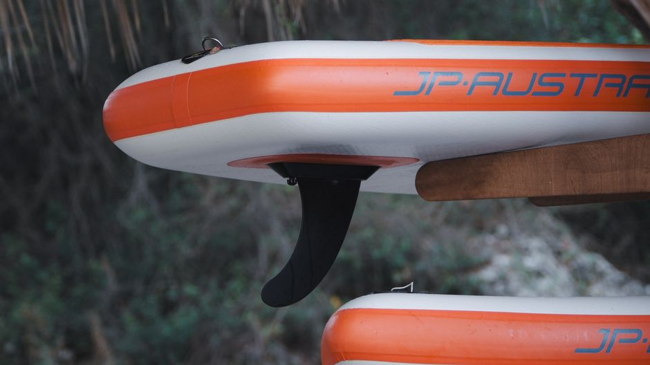 A detailed view of an orange and white inflatable paddleboard featuring its fin.
