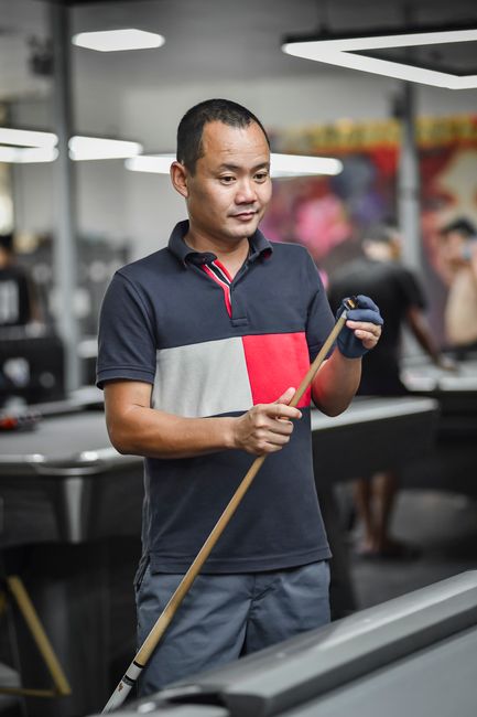 Man holding a pool cue in a modern indoor pool hall in Hanoi, Vietnam.