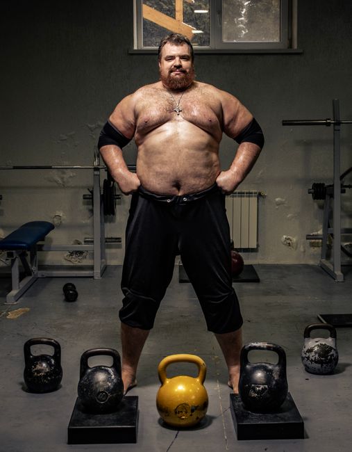 Muscular man shirtless in gym with kettlebells showcasing strength. Indoor workout concept.