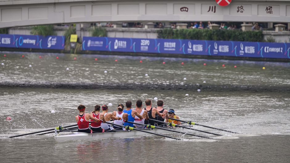 Rowing team in competitive race under bridge during a sports event.