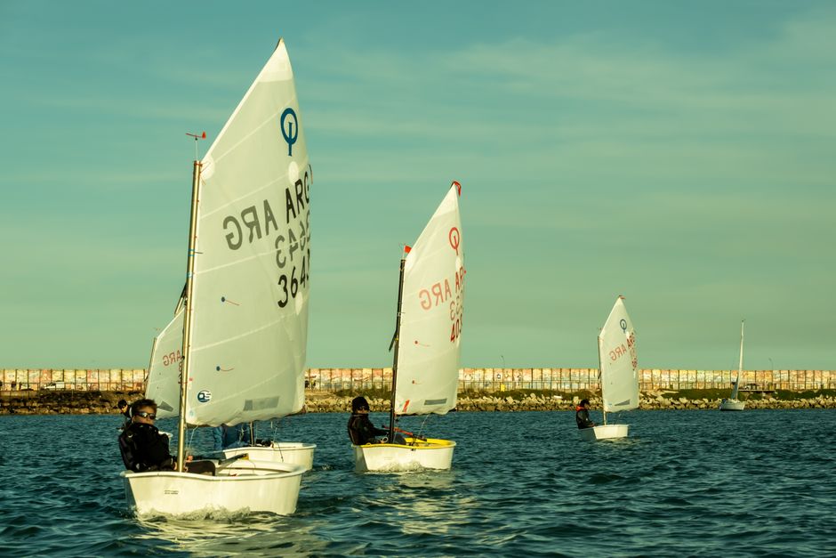 Young sailors in Optimist dinghies racing on the ocean, capturing a sunny day outdoors.