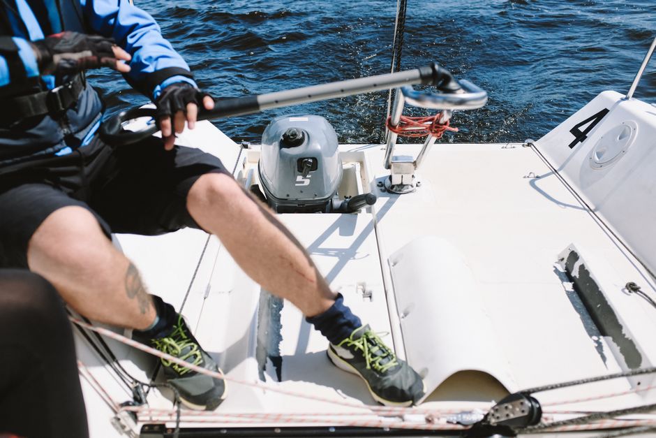 Close-up of a yachtsman steering a yacht with a tiller on open water, ideal for sailing enthusiasts.