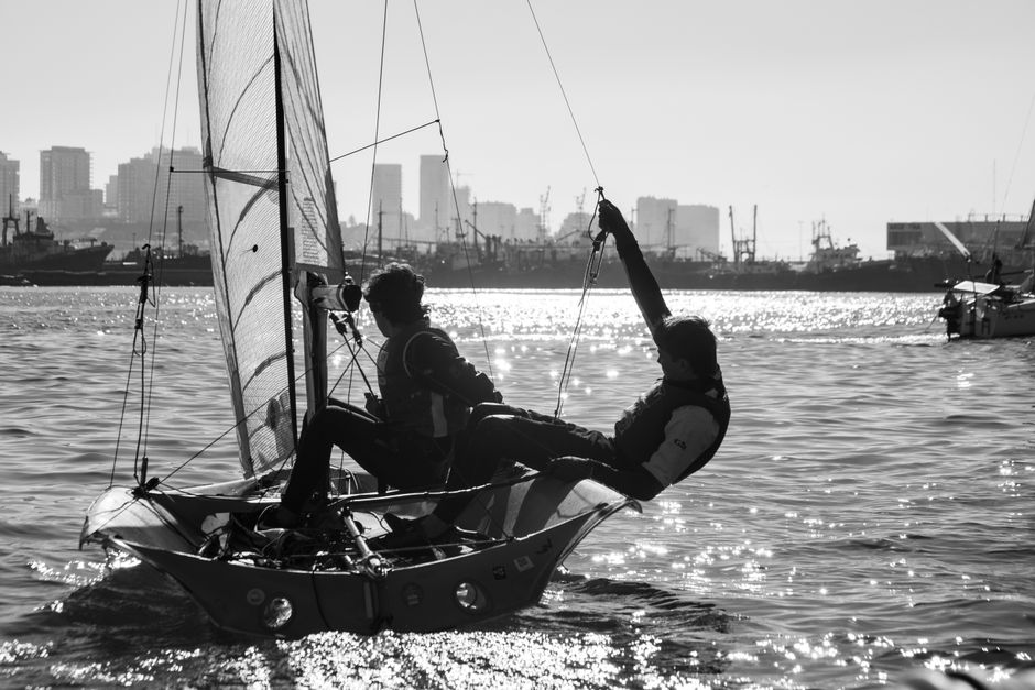 Two people sailing a sailboat on the ocean against the skyline of Mar del Plata, Argentina.