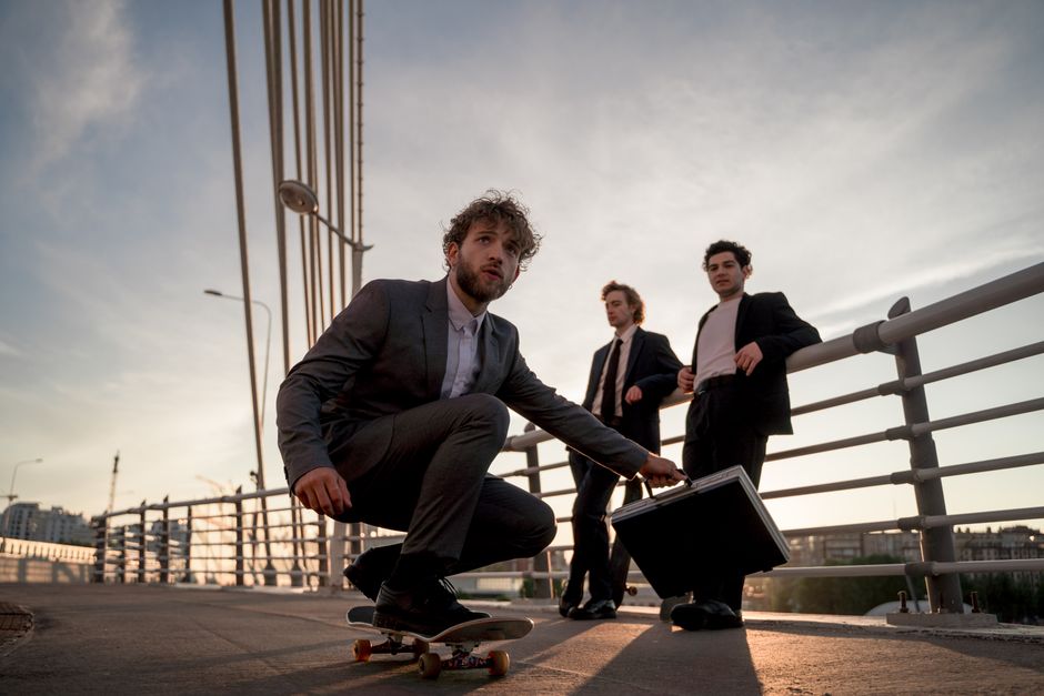 Three young businessmen in suits, skateboarding on a city bridge at sunset, exuding a modern and dynamic lifestyle.