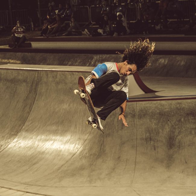 Skateboarder performing an aerial trick at night in an urban skate park.