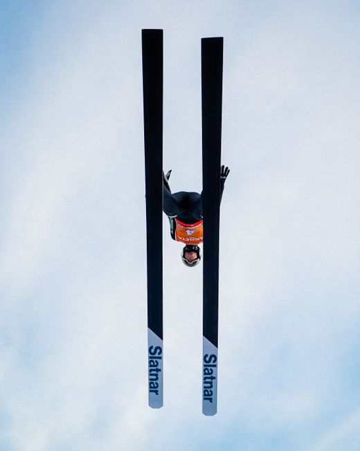 A ski jumper captured in mid-air against a clear sky, showcasing athleticism in a winter sport.