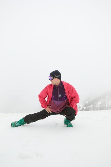 A man in winter clothing stretches on a snow-covered mountain, preparing for activity.