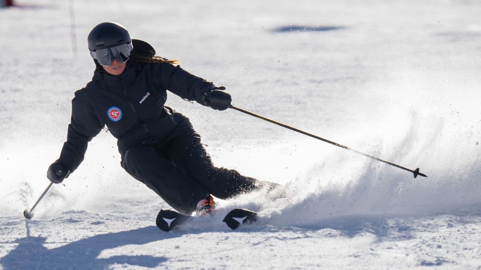Skier in black gear skillfully turns on snowy slope under bright daylight.