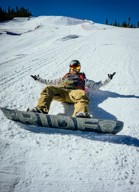 A snowboarder rests on a snowy slope, enjoying a bright day outdoors.