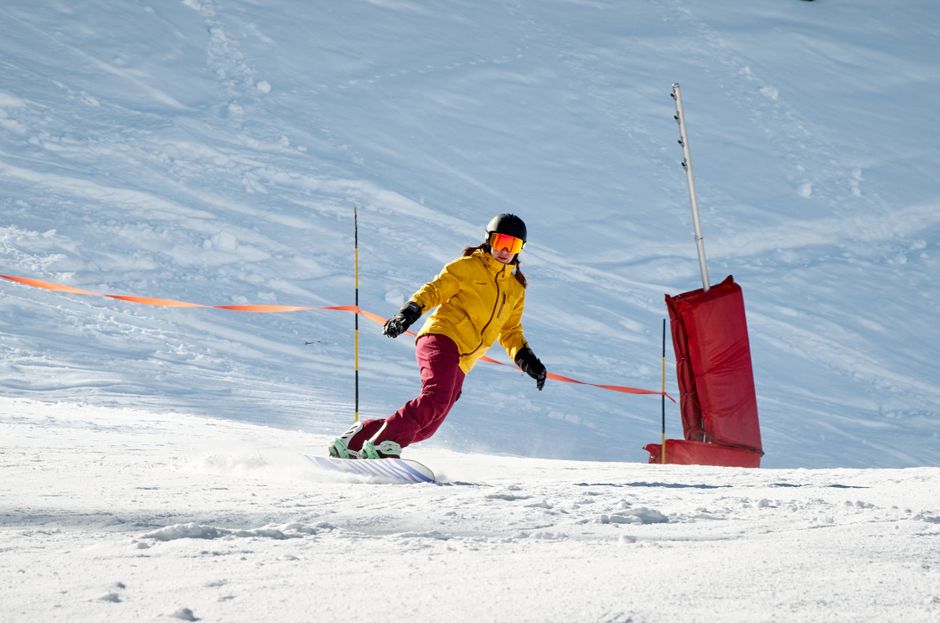 Snowboarder in vibrant gear carving on a sunny winter day.