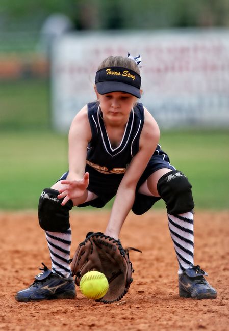 Young girl in uniform playing softball outdoors, catching a ball on the field.