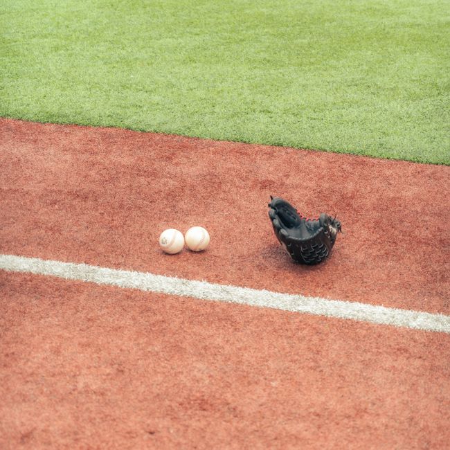 A baseball glove and two balls on a grassy turf field, ready for play.