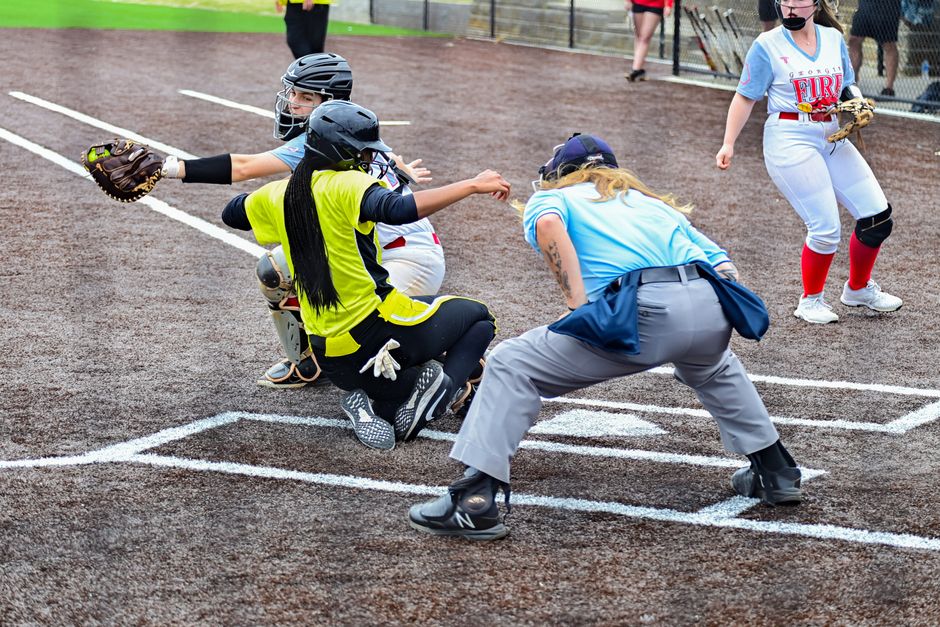 Dramatic action shot of a softball player sliding into home plate during a game.