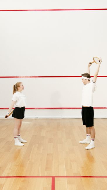 A man and woman in sportswear exercise with squash rackets on an indoor court.