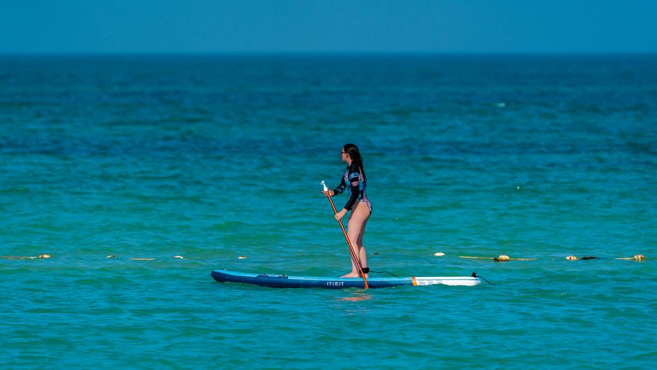 Side view of distant unrecognizable female surfer in wetsuit standing on paddleboard in rippling sea on summer day in nature