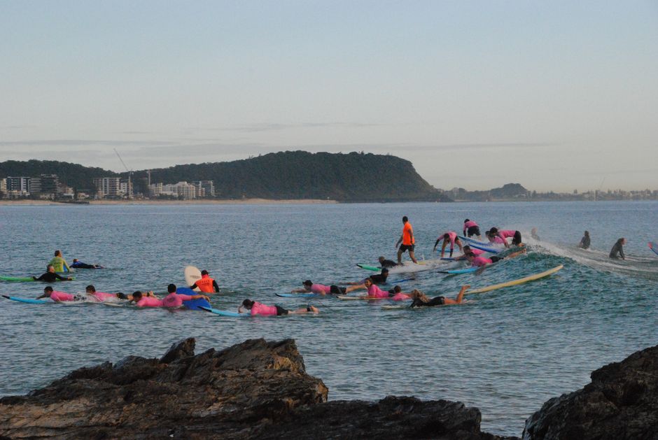Surfing group lesson near scenic coastline, vibrant attire, dynamic formations.
