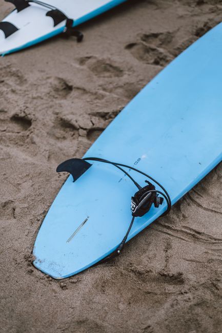 Close-up view of a blue surfboard resting on a sandy beach, depicting a simple, coastal lifestyle.