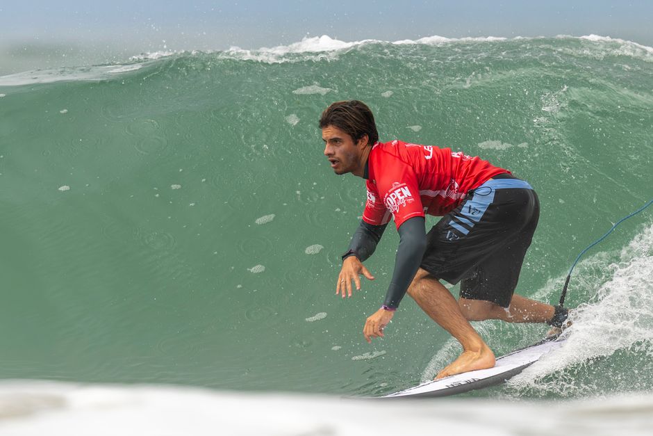 A skilled surfer in a red jersey expertly rides a large wave showcasing dynamic movement and balance.