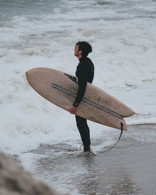 A surfer stands with a board at the ocean's edge, ready for the waves.