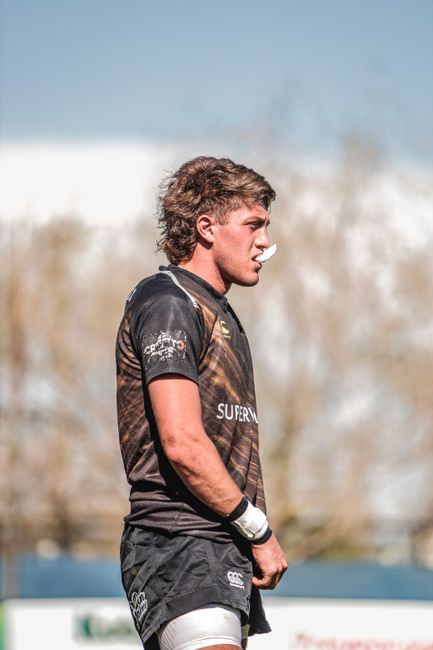 Focused rugby player with a mouthguard on the field, under clear skies.