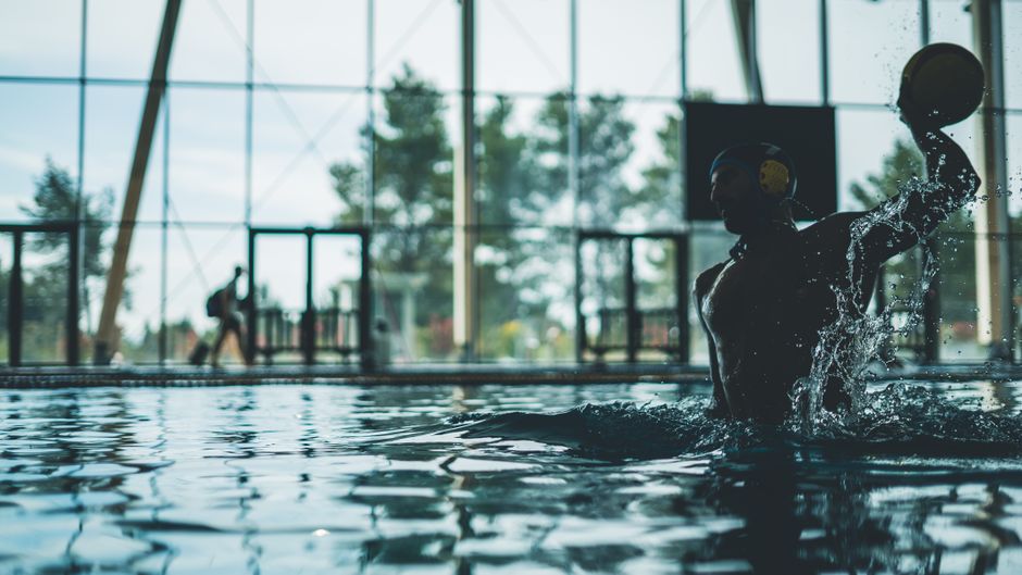 Athlete playing water polo indoors with water splash in a dynamic action shot.